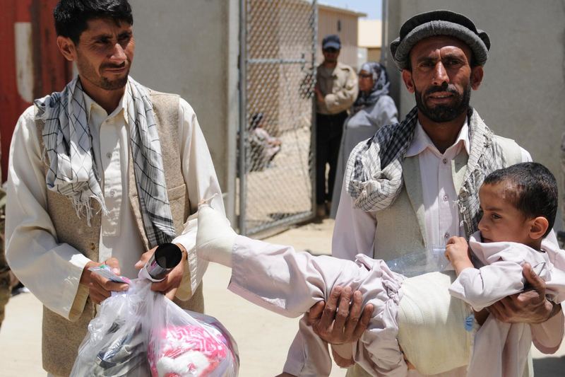 Afghan men, with a bandanged-up child in tote, leave the Egyptian Hospital on Bagram Airfield with donated care packages from Operation Care May 29. Coalition f